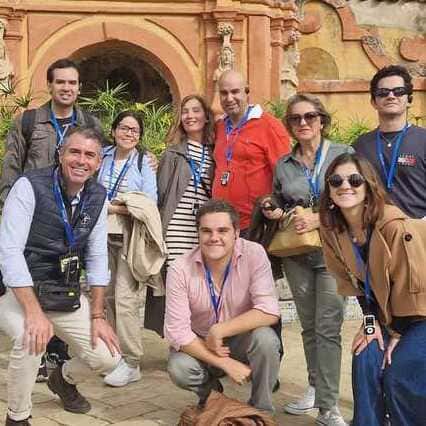 The photo captures a group of friends and our guide posing for a photo in the historical garden setting of the Alcazar Seville during one of our Seville Private Tours. The group comprises a mix of standing and crouching individuals dressed in casual to smart-casual attire. In the background, a well-manicured garden with a statue showcases the ornate style of the Alcazar Seville Gardens, reflecting the rich historical and cultural essence of the location.